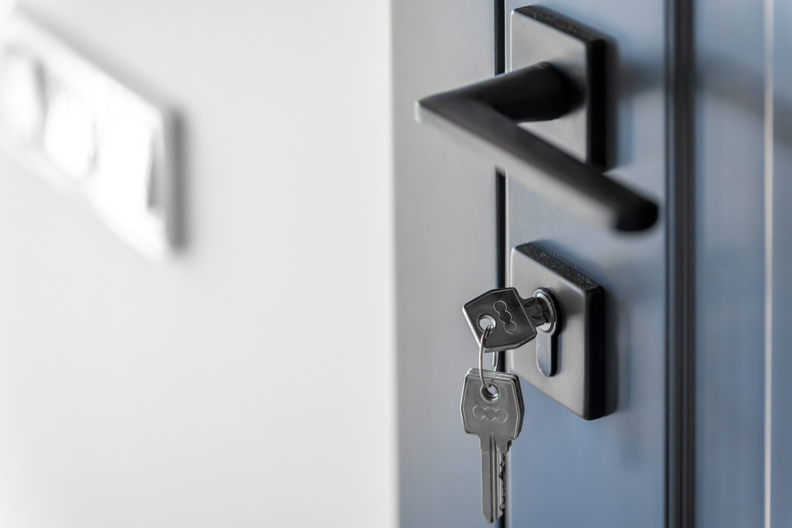 Keys in the cylinder of a matte blue door beside a slim black handle, soft light and generous copy space create a calm modern scene.